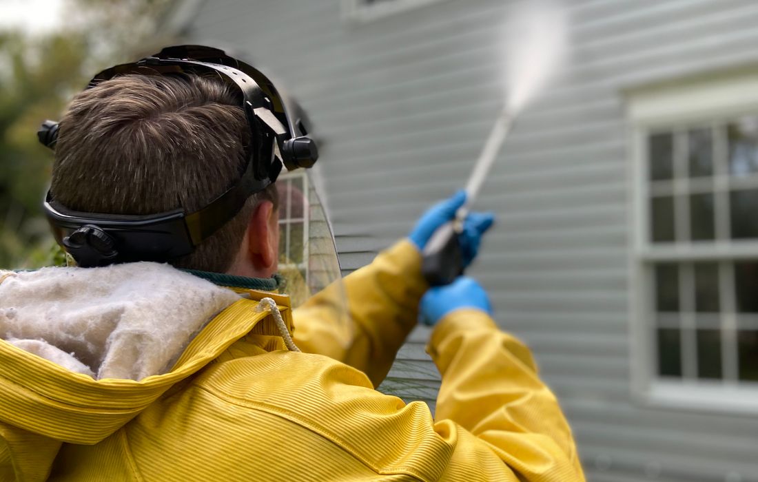 Technician in protective gear pressure washing house siding